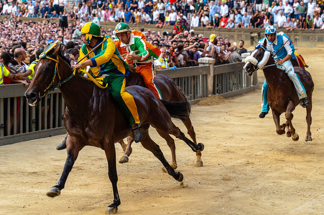 Jockeys in farbenfrohen Outfits, die ihre jeweiligen Nachbarschaften repräsentieren (contrade), wetteifern um die Führung im Palio, Siena, Toskana, Italien, Europa