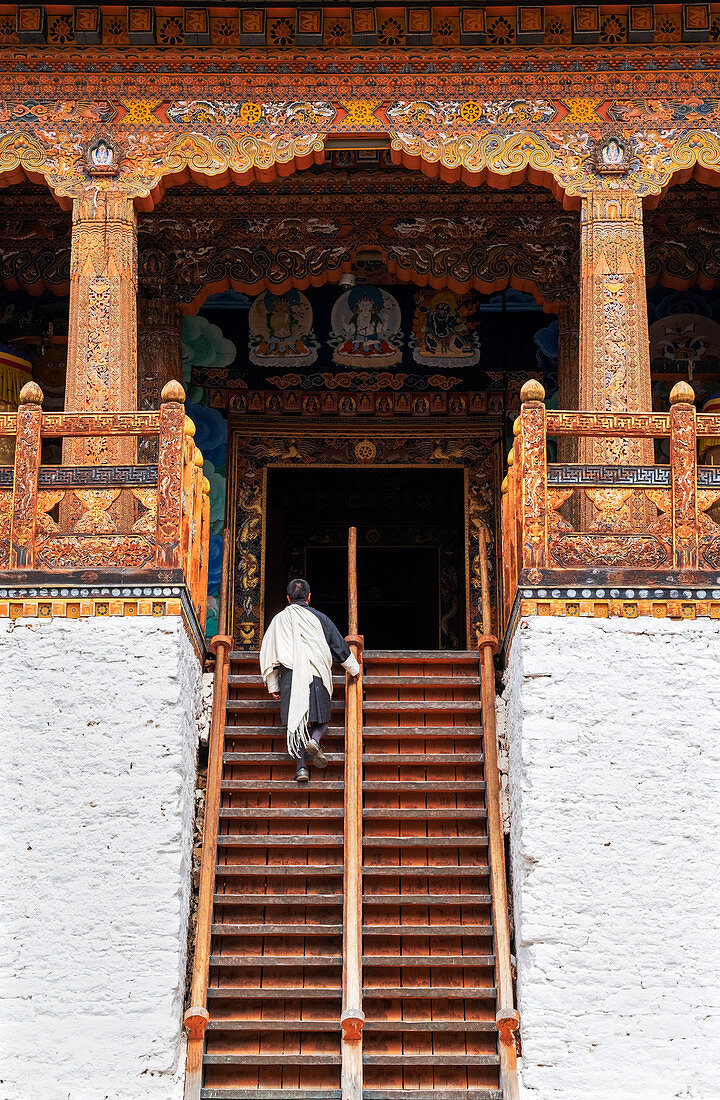Bhutanischer Mann in traditioneller Kleidung, die Treppen in Tempel, Punakha Dzong, Bhutan, Asien klettert
