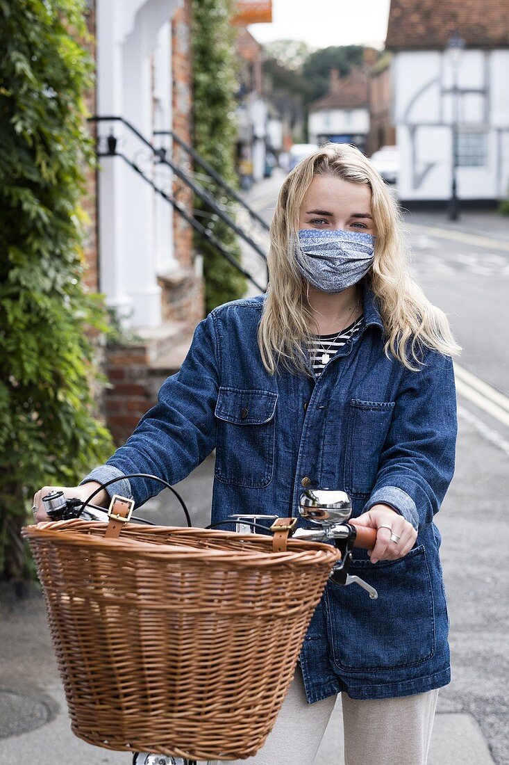 Junge blonde Frau mit Gesichtsmaske schiebt Fahrrad mit Korb