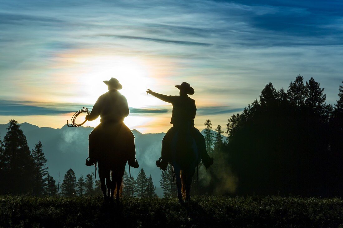 Zwei Cowboys reiten über Grasland mit Bergen im Hintergrund, am frühen Morgen