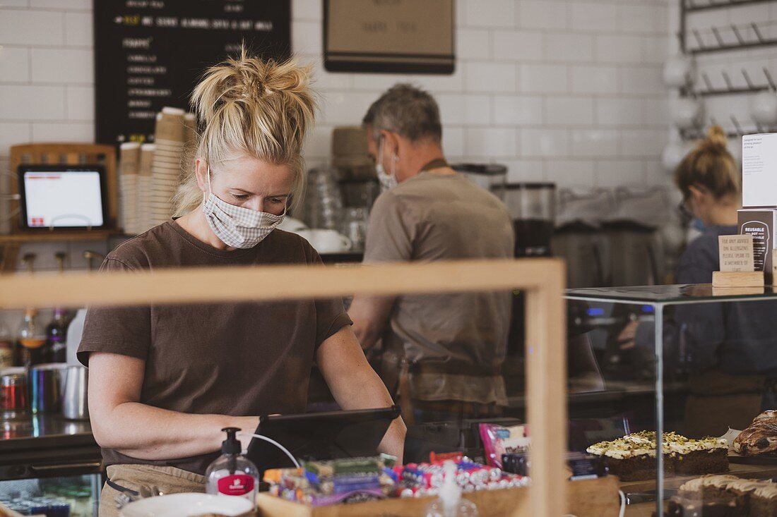 Blond waitress wearing face mask working in a cafe.