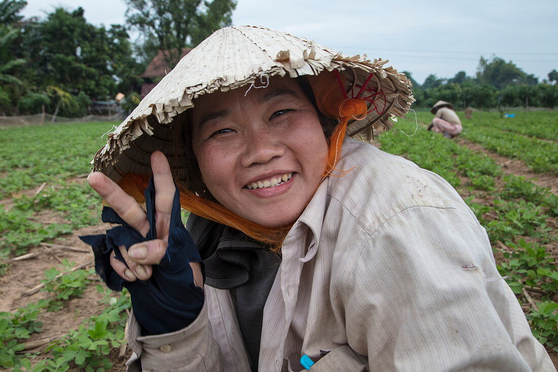 Porträt einer keck schauenden vietnamesischen Frau die konischen Hut trägt und in einem Erdnussfeld arbeitet, My Luong Canal, Fluss Mekong, nahe My An Hung, An Giang, Vietnam, Asien