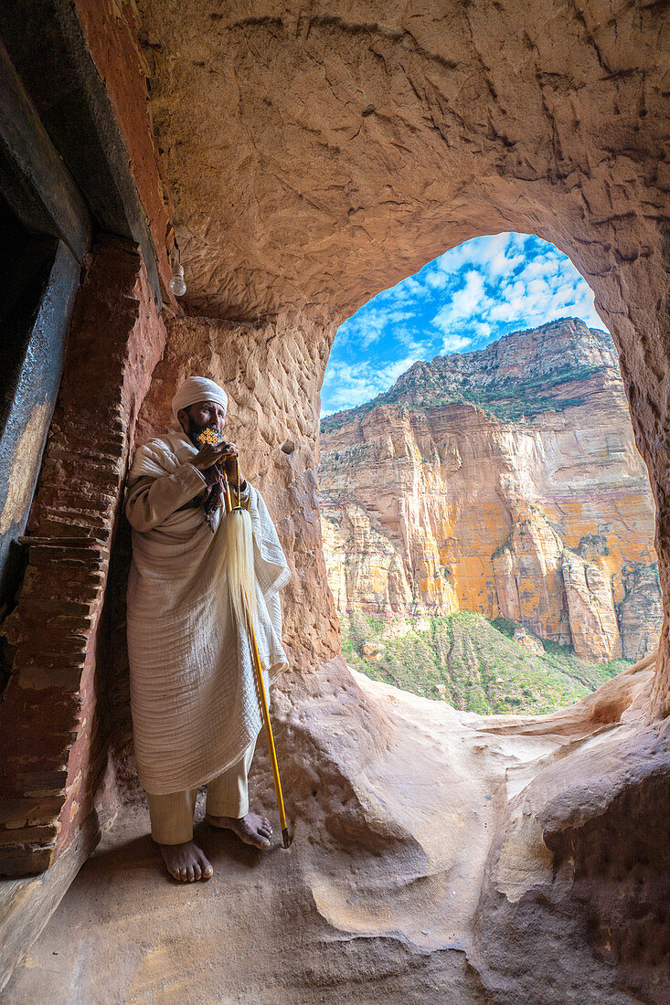 Äthiopischer orthodoxer Priester, der das Handkreuz am Eingang der Abuna Yemata Guh Kirche, Gheralta Berge, Tigray, Äthiopien, Afrika hält