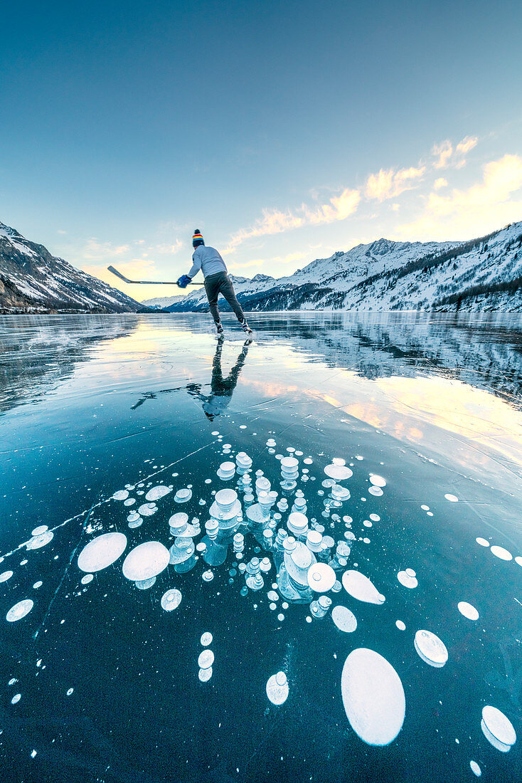 Ice hockey player skating on frozen Lake Sils covered of bubbles, Engadine, canton of Graubunden, Switzerland, Europe