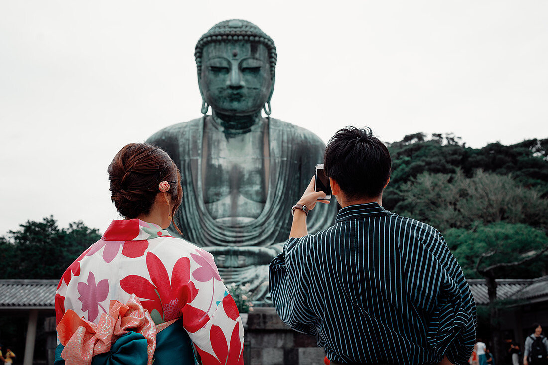Koutokuin Temple with couple in foreground taking a photo of Buddha statue, Toyko, Japan