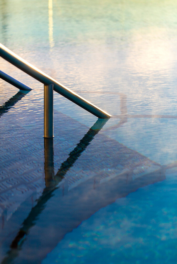 Detail shot of railing going into water in exterior pool, with morning steam. Bath, United Kingdom