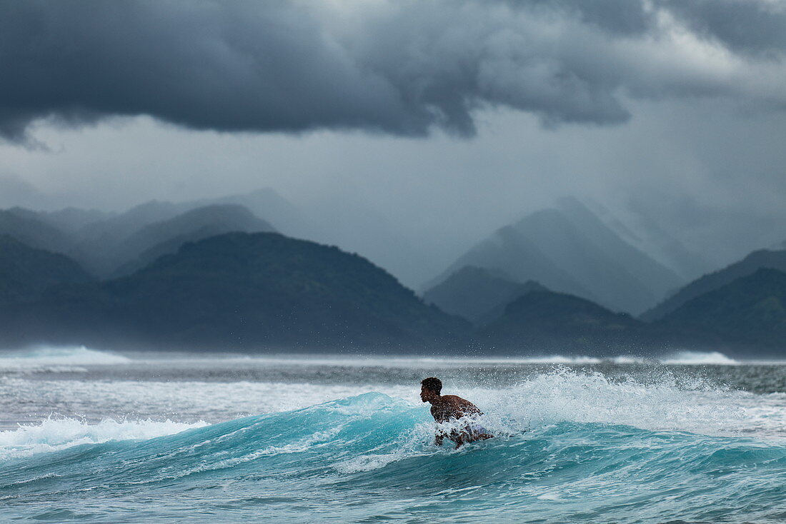 Surfer auf Welle im Surfgebiet Teahupoo mit Gewitterwolken und Bergen dahinter, Tahiti Iti, Tahiti, Windward Islands, Französisch-Polynesien, Südpazifik