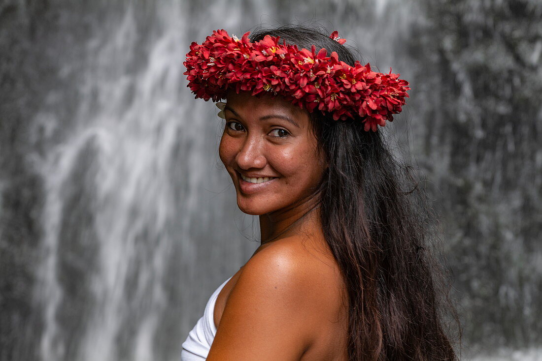 Porträt einer hübschen jungen Tahitianerin mit Blumenkopfschmuck vor Wasserfall in "The Water Gardens of Vaipahi", Teva I Uta, Tahiti, Windward Islands, Französisch-Polynesien, Südpazifik