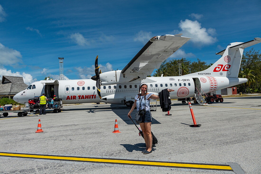Lächelnde Frau mit Kamera verlässt Air Tahiti ATR 72-600 Flugzeug auf Vorfeld von Flughafen Bora Bora (BOB), Bora Bora, Leeward Islands, Französisch-Polynesien, Südpazifik