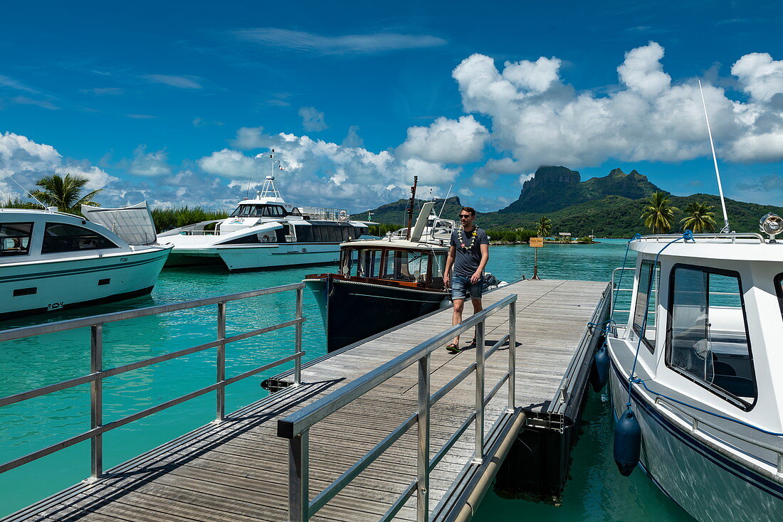 Junger Mann läuft entlang Pier von Bora Bora Flughafen (BOB) mit Booten und Mount Otemanu in der Ferne, Bora Bora, Leeward Islands, Französisch-Polynesien, Südpazifik