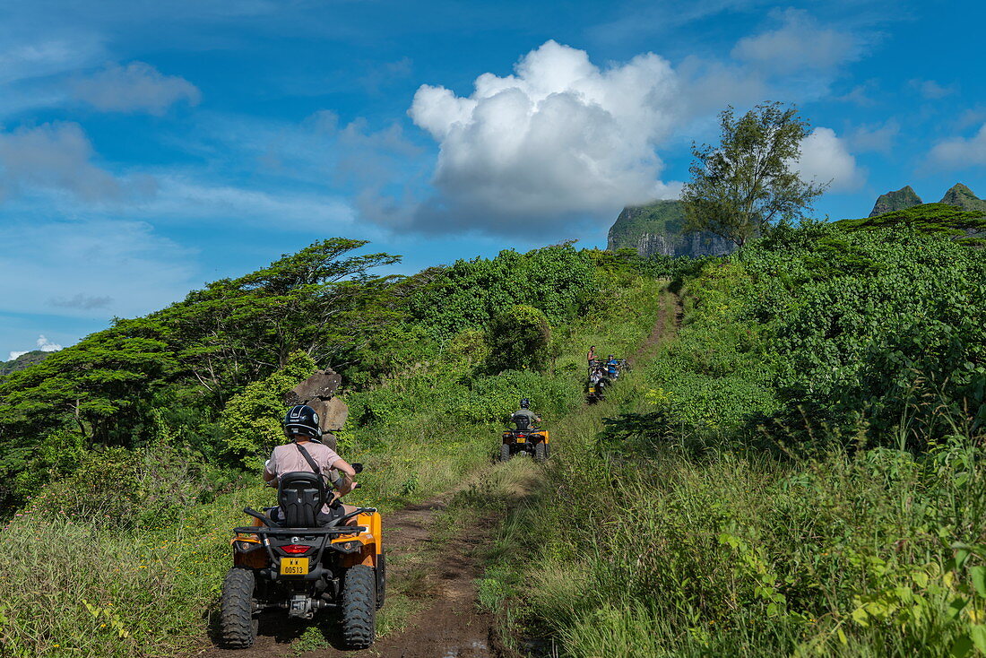 Menschen beim Ausflug mit Quad Geländefahrzeug auf unbefestigter Straße durch üppige Bergvegetation, Bora Bora, Leeward Islands, Französisch-Polynesien, Südpazifik