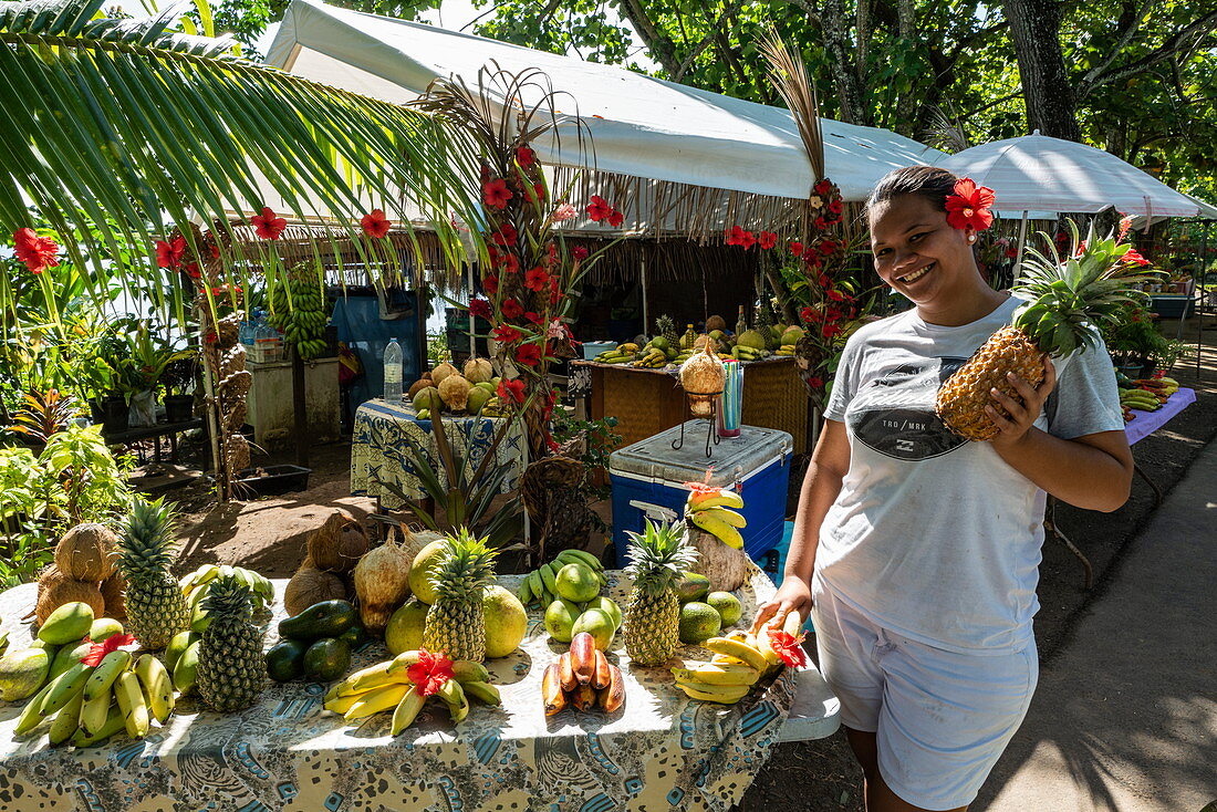 Eine junge Frau mit Obst und Gemüse zum Verkauf an einem Marktstand am Straßenrand, Apootaata, Moorea, Windward Islands, Französisch-Polynesien, Südpazifik