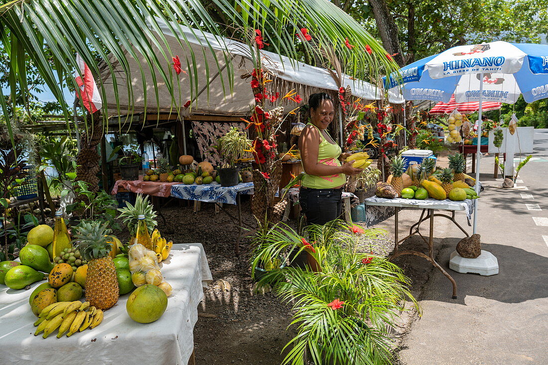 Frau verkauft tropische Früchte an einem Obst- und Gemüsestand am Straßenrand in Papetoai, Moorea, Windward Islands, Französisch-Polynesien, Südpazifik
