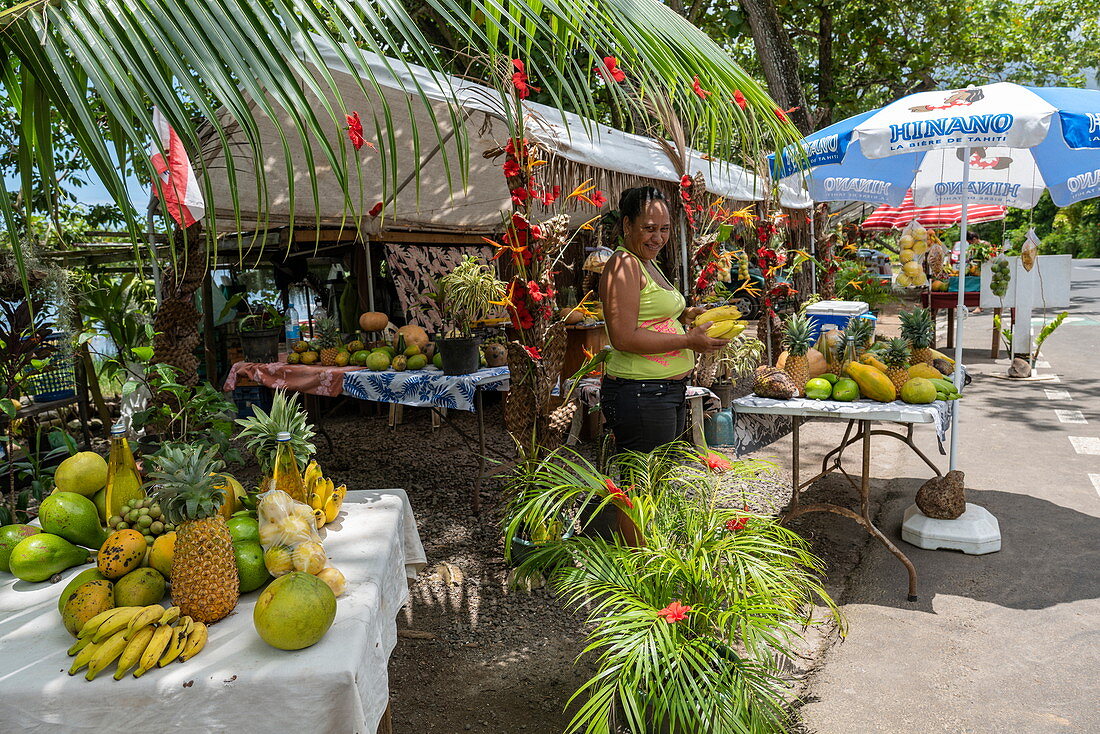 Woman sells tropical fruits at a roadside fruit and vegetable stand in Papetoai, Moorea, Windward Islands, French Polynesia, South Pacific