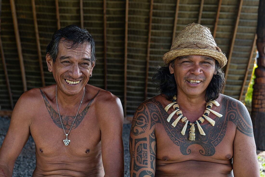 Zwei Männer mit Tätowierungen - einer mit Kette aus geschnitzten Walknochen - lächeln im Kulturzentrum Te Tumu in die Kamera, Tekoapa, Ua Huka, Marquesas-Inseln, Französisch-Polynesien, Südpazifik