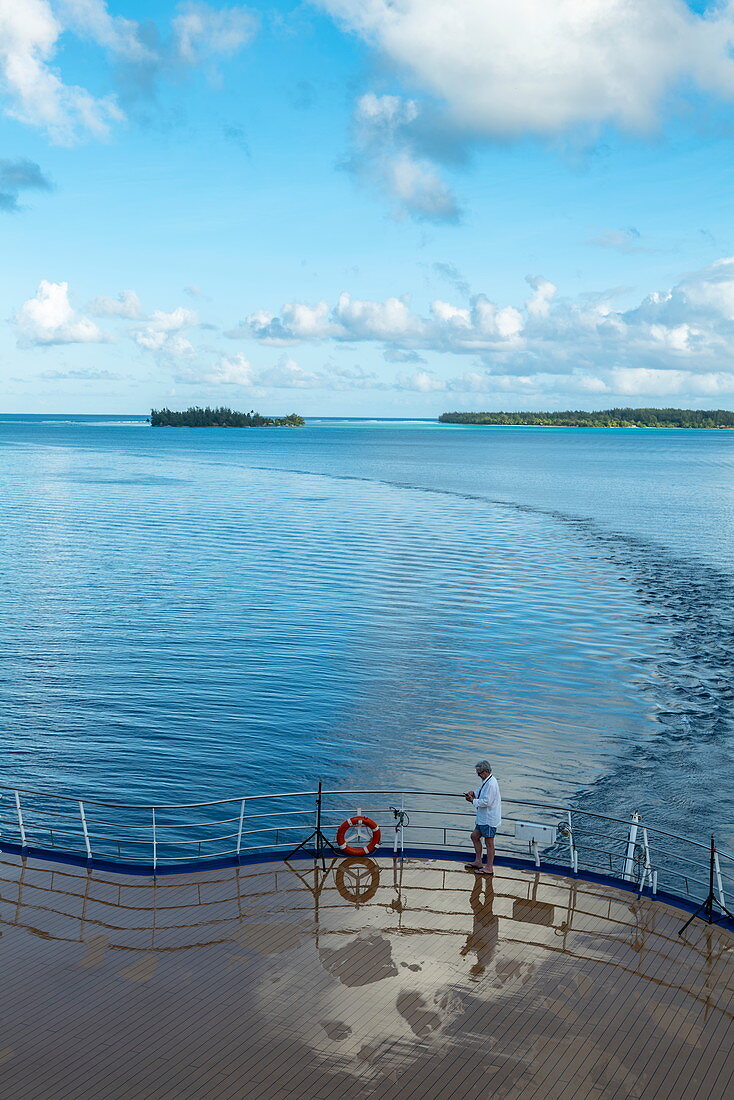 Mann auf dem hinteren Sonnendeck von Passagierfrachtschiff Aranui 5 (Aranui Cruises) nach Durchfahrt durch den Kanal in die Lagune von Bora Bora, Bora Bora, Leeward Islands, Französisch-Polynesien, Südpazifik