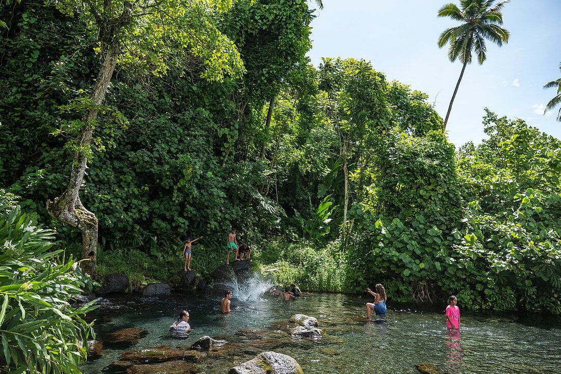 Menschen entspannen sich in einem Fluss mit Wasserfall inmitten üppiger Vegetation, nahe Taravao, Tahiti, Windward Islands, Französisch-Polynesien, Südpazifik