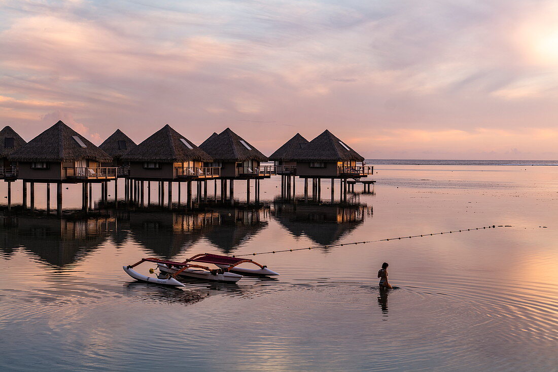 Silhouette of woman in the water next to the outrigger canoe and overwater bungalows of the Tahiti Ia Ora Beach Resort (managed by Sofitel) at sunset, near Papeete, Tahiti, Windward Islands, French Polynesia, South Pacific