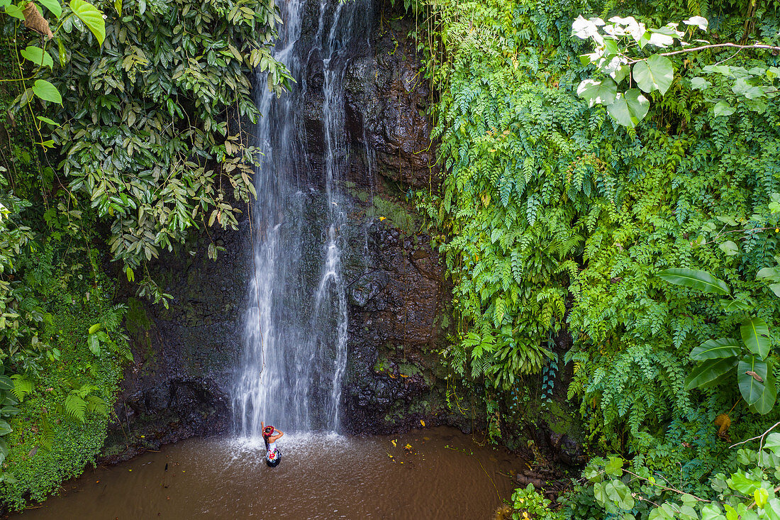 Luftaufnahme einer schönen jungen Tahitianerin die vor Wasserfall in "The Water Gardens of Vaipahi" tanzt, Teva I Uta, Tahiti, Windward Islands, Französisch-Polynesien, Südpazifik tanzt