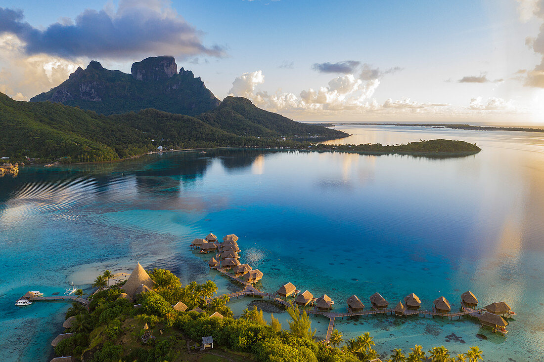 Luftaufnahme des Sofitel Bora Bora Private Island Resort mit Überwasserbungalows in der Lagune von Bora Bora mit Mount Otemanu bei Sonnenaufgang, Vaitape, Bora Bora, Leeward Islands, Französisch-Polynesien, Südpazifik