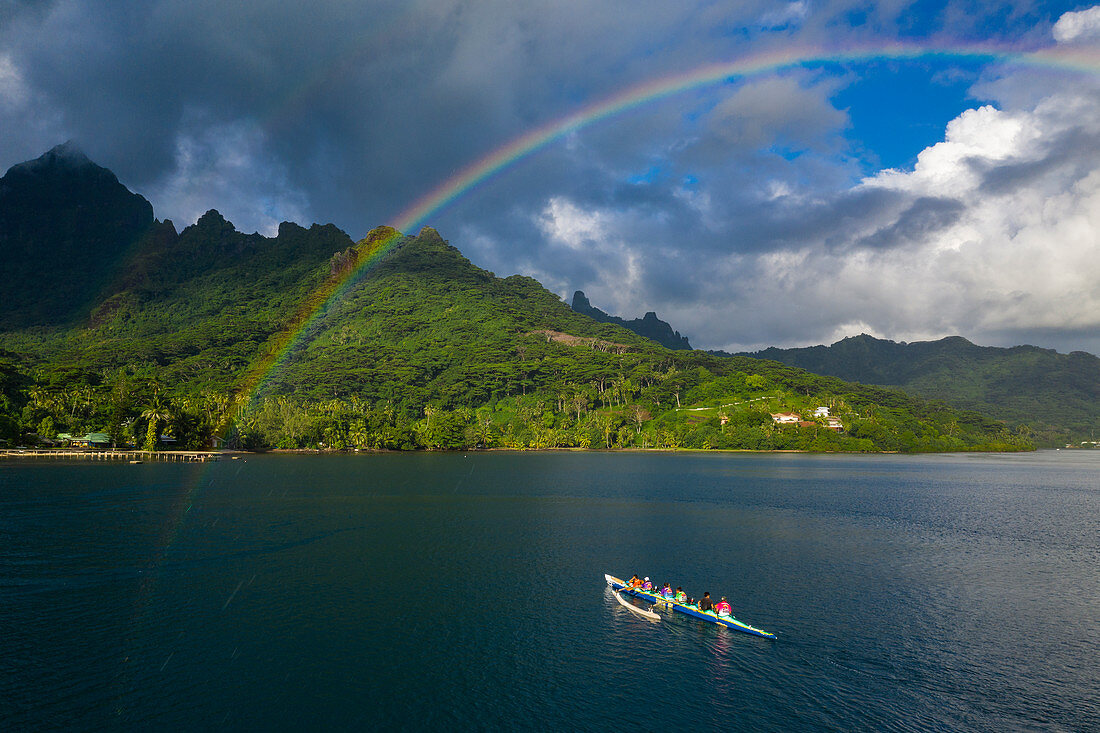 Aerial view of outrigger racing canoe in the Moorea Lagoon with rainbow and mountain backdrop, Avamotu, Moorea, Windward Islands, French Polynesia, South Pacific