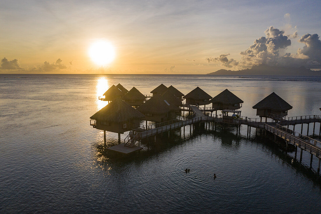 Luftaufnahme von Überwasserbungalows des Tahiti Ia Ora Beach Resort (managed by Sofitel) bei Sonnenuntergang mit Insel Moorea in der Ferne, nahe Papeete, Tahiti, Windward Islands, Französisch-Polynesien, Südpazifik