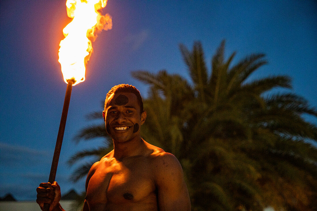Freundlicher fidschianischer "Krieger" mit Fackel zum Anzünden von Tiki Fackeln im Pullman Nadi Bay Resort & Spa in der Abenddämmerung, Nadi, Viti Levu, Fidschi-Inseln, Südpazifik
