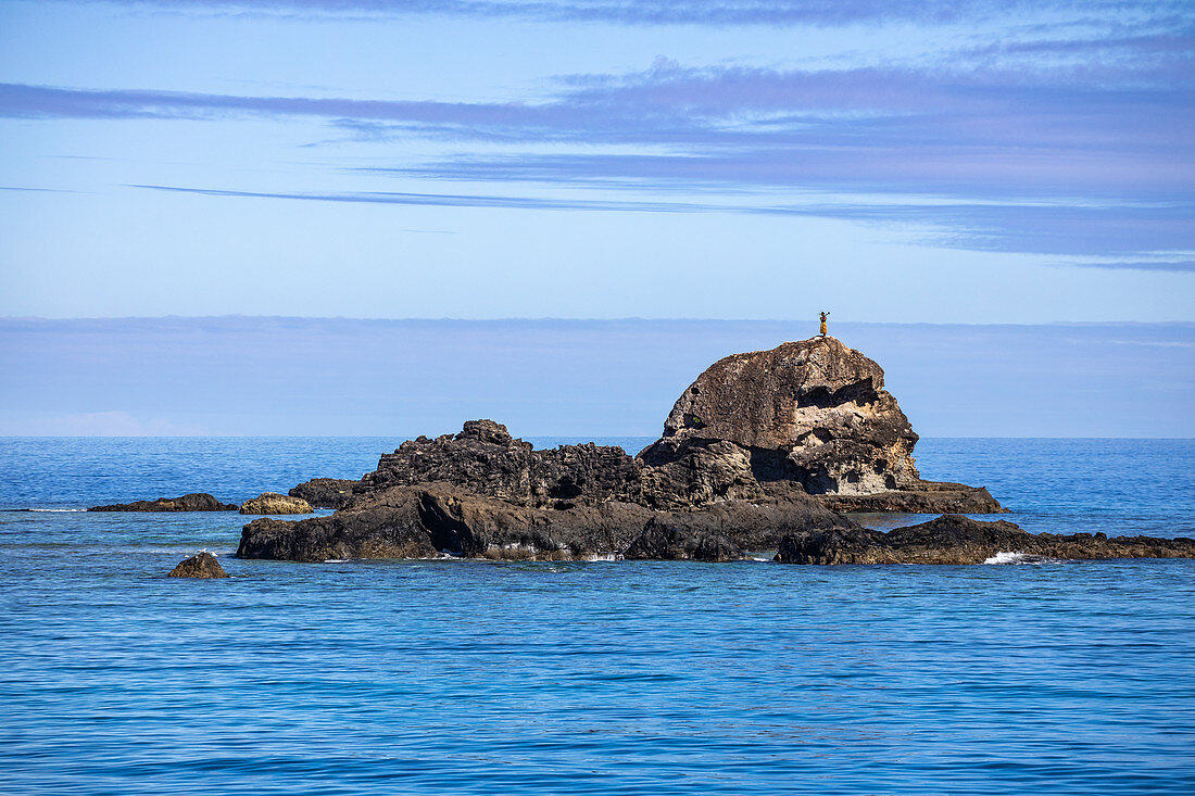 Ein Fidschianer steht auf einem Felsen und heißt Passagiere des Katamaran Yasawa Flyer II (South Sea Cruises) bei Annäherung an die Yasawa Inselgruppe auf traditionelle Art willkommen, Kuata Island, Yasawa Group, Fidschi-Inseln, Südpazifik