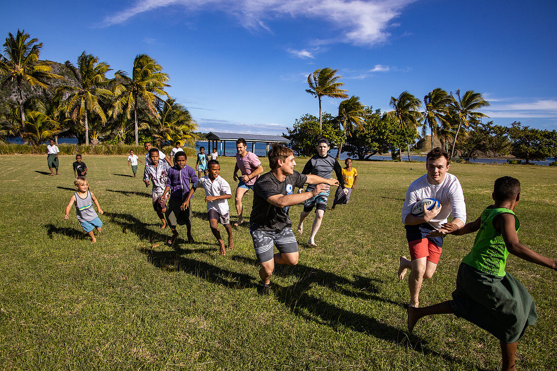 Passagiere von Kreuzfahrtschiff MV Reef Endeavour (Captain Cook Cruises Fiji) spielen Rugby mit einheimischen Jungen auf dem Feld der Dorfschule, Nabukeru, Yasawa Island, Yasawa Group, Fidschi-Inseln, Südpazifik