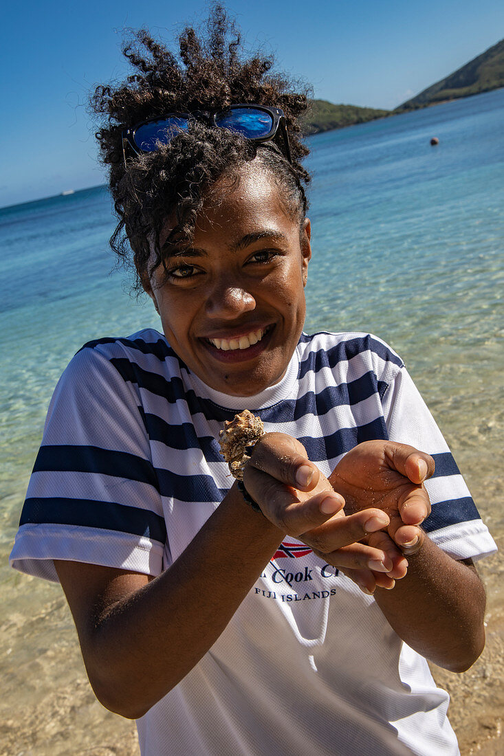 Happy crew member of cruise ship MV Reef Endeavor (Captain Cook Cruises Fiji) holds hermit crab in hands, Yaqeta, Yangetta Island, Yasawa Group, Fiji Islands, South Pacific