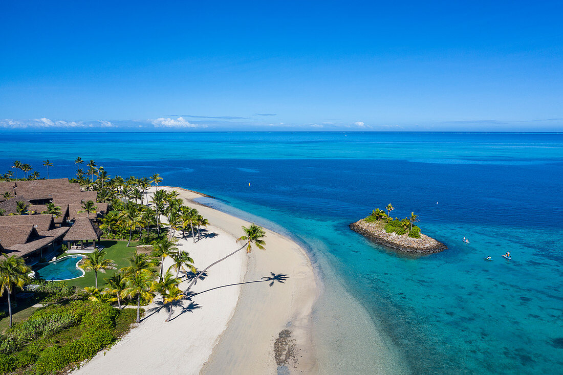 Luftaufnahme einer Residence Villa Unterkunft im Six Senses Fiji Resort mit Kokospalmen, Strand und einer Familie die Wassersport Aktivitäten neben kleiner vorgelagerter Insel genießt, Malolo Island , Mamanuca Group, Fidschi-Inseln, Südpazifik