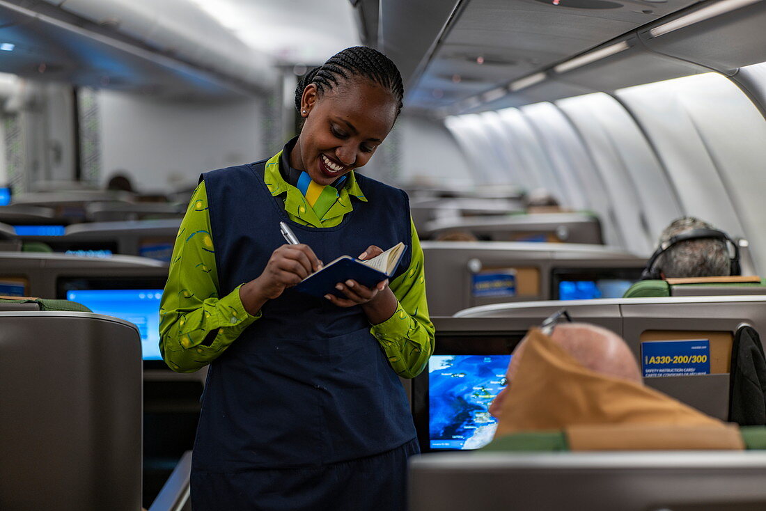 Lächelnde Flugbegleiterin nimmt die Essensbestellung von einem Passagier in der Business Class an Bord eines RwandAir Airbus A330-300 Flugzeug entgegen, auf dem Flug vom internationalen Flughafen Brüssel (BRU) in Belgien zum internationalen Flughafen Kigali (KIG) in Ruanda, Afrika