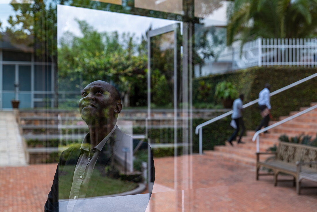 Nachdenklich blickender ruandischer Mann und Spiegelung in Fenster am Kigali Genocide Memorial Center, Kigali, Kigali Province, Ruanda, Afrika