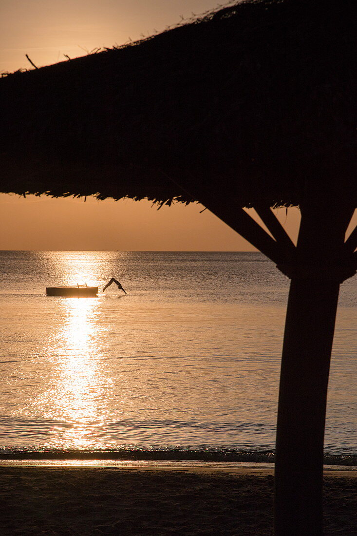 Silhouette von strohgedeckten Sonnenschirm und junger Frau die von Badeplattform ins Wasser vor dem Ong Lang Beach springt, Ong Lang, Insel Phu Quoc, Kien Giang, Vietnam, Asien