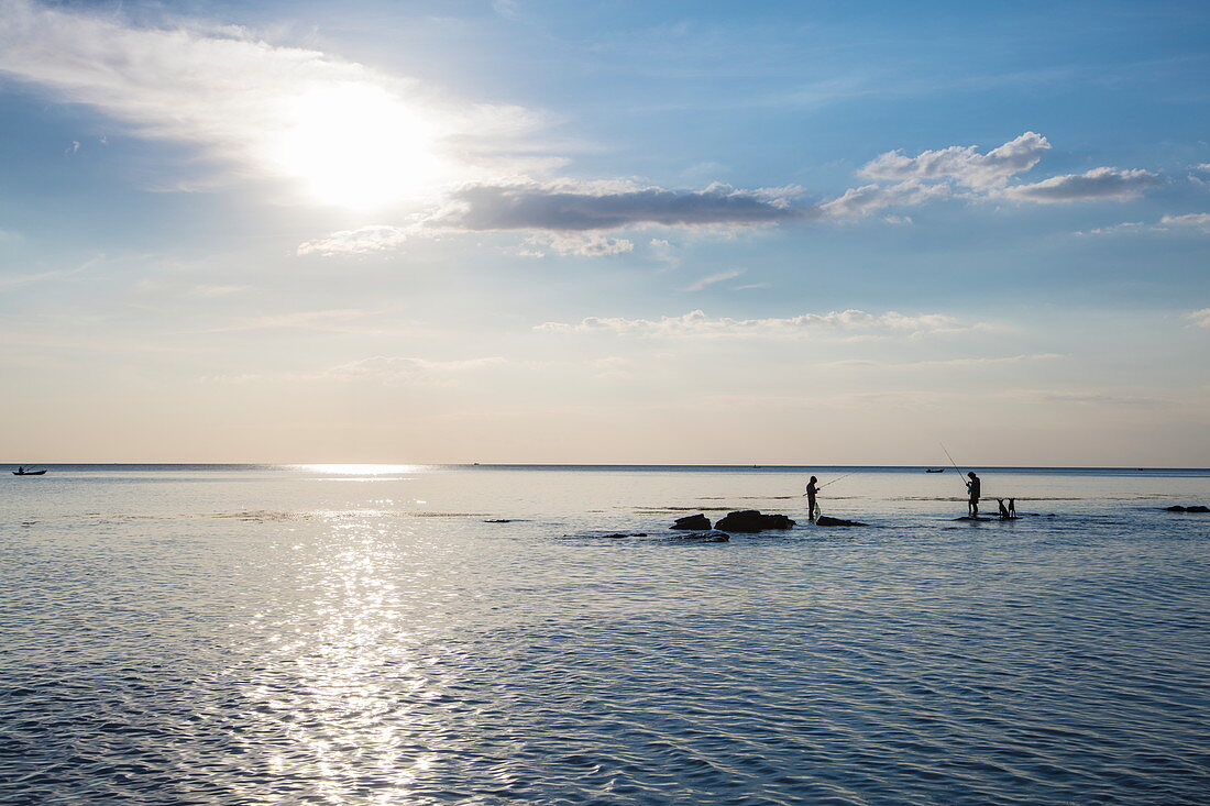 Silhouette von zwei Fischern und Hunden die auf Felsen im Wasser vor dem Ong Lang Beach stehen, Ong Lang, Insel Phu Quoc, Kien Giang, Vietnam, Asien
