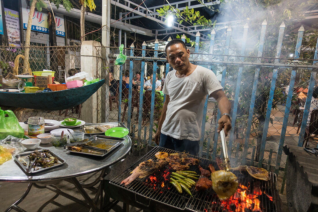 Mann grillt frischen Fisch, Fleisch und Gemüse bei No Name BBQ im Ong Lang Village, Ong Lang, Insel Phu Quoc, Kien Giang, Vietnam, Asien