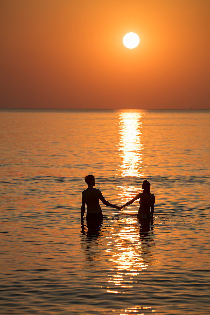 Silhouette of a romantic young couple holding hands in the water in front of Ong Lang Beach at sunset, Ong Lang, Phu Quoc Island, Kien Giang, Vietnam, Asia