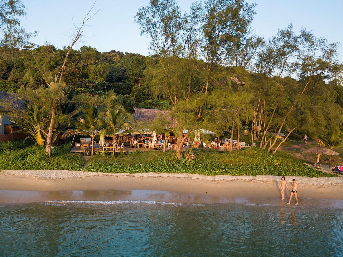 Luftaufnahme von jungem Paar das entlang Ong Lang Beach spaziert mit Restaurant und Bar des Mango Bay Resort dahinter, Ong Lang, Insel Phu Quoc, Kien Giang, Vietnam, Asien