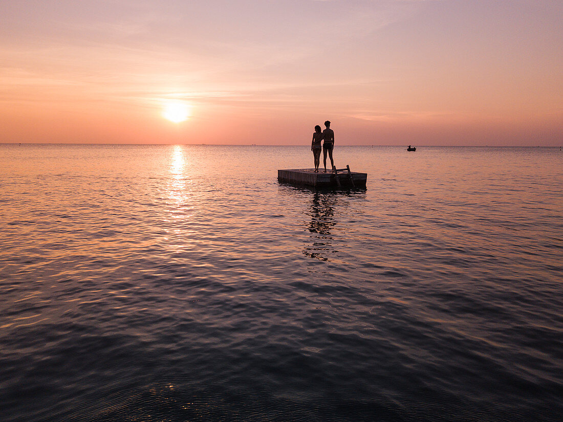 Luftaufnahme Silhouette von jungem Paar das bei Sonnenuntergang auf einer Badeplattform am Ong Lang Beach steht, Ong Lang, Insel Phu Quoc, Kien Giang, Vietnam, Asien