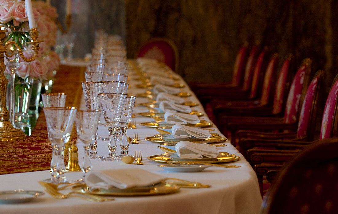 A table set with gold plates and gold gutlery and crystal glasses. Shot in Madrid, Spain.