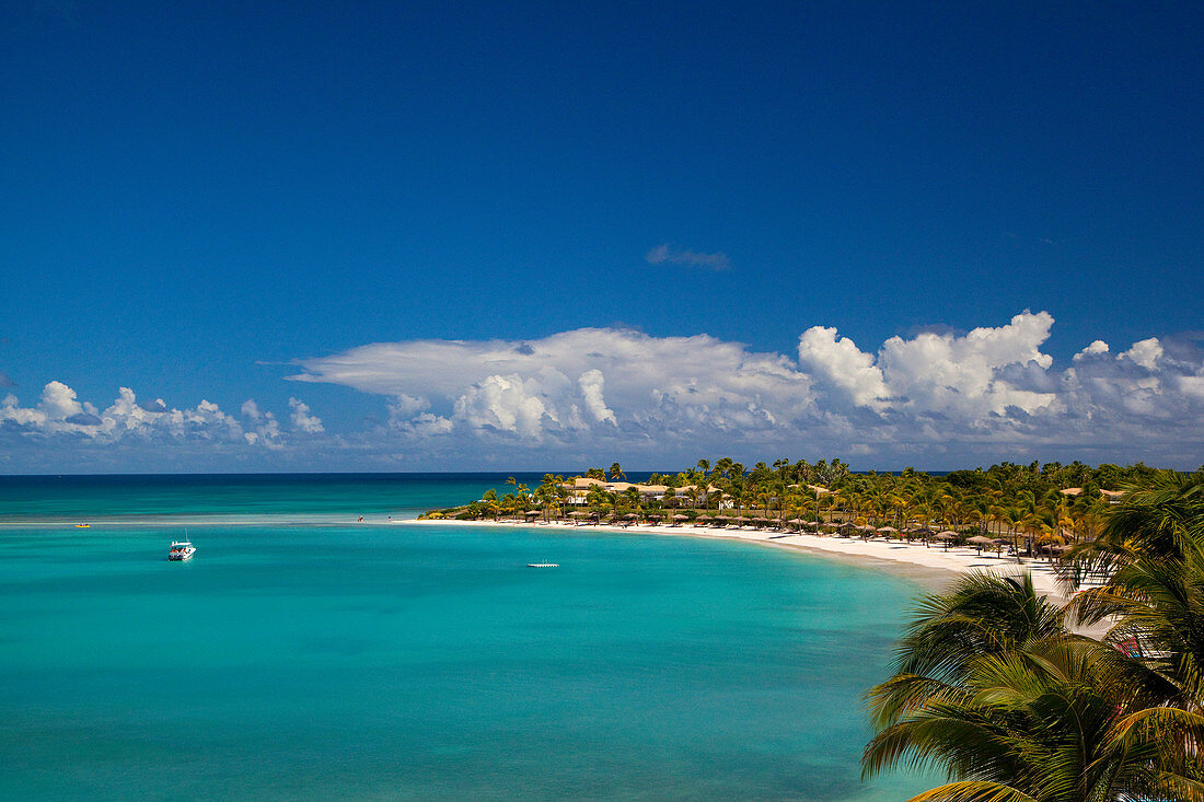 A shot of a bay, with bright turqoise waters and a white sandy beach and a blue sky with white clouds. Antigua.