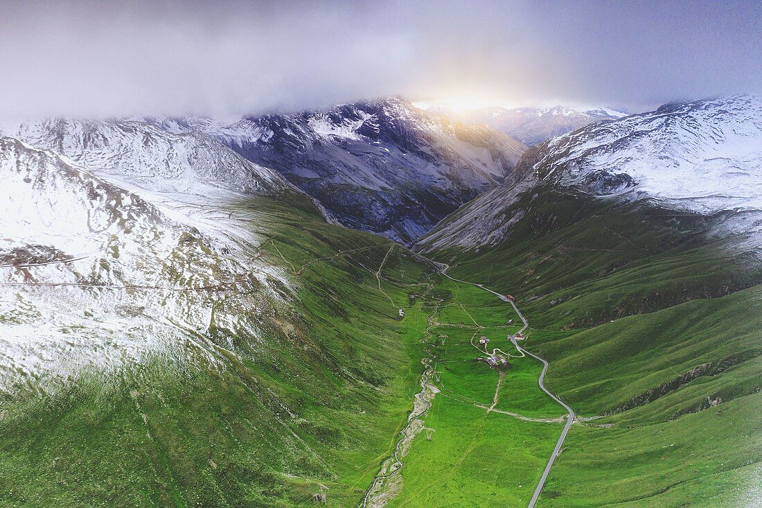 Green meadows framed by snow capped mountains in spring, aerial view, Braulio Valley, Bormio, Valtellina, Lombardy, Italy