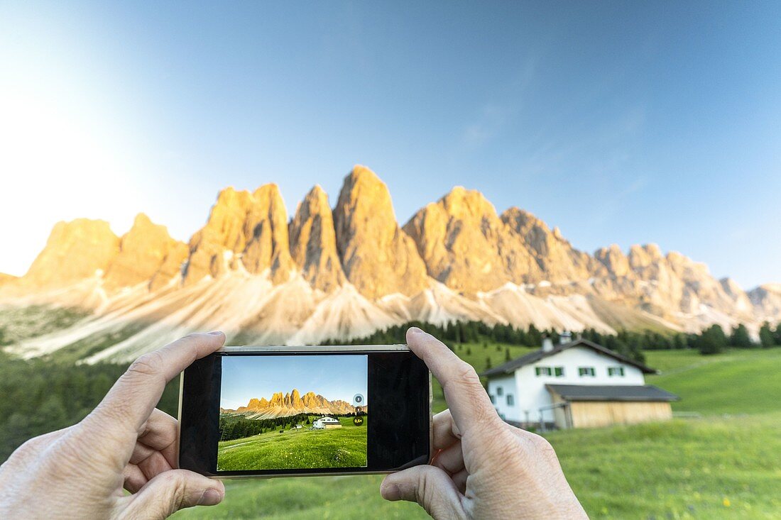 Persönliche Perspektive des Touristen, der die Odle mit Smartphone bei Sonnenuntergang, Val di Funes, Südtirol, Dolomiten, Italien fotografiert