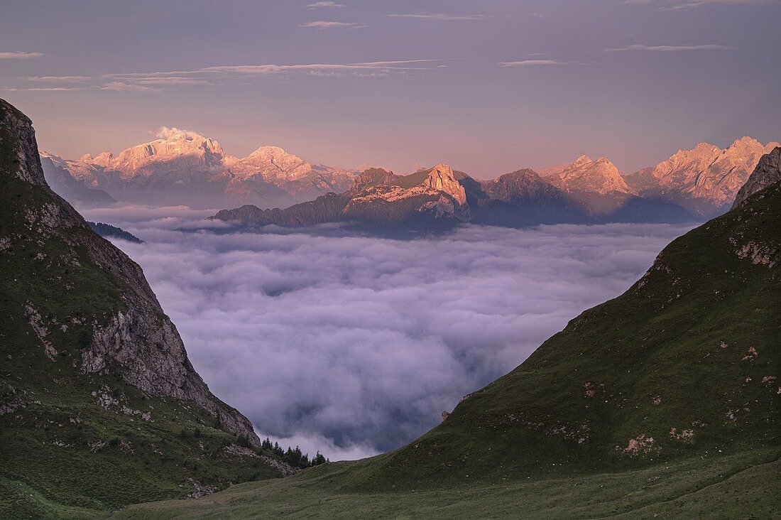 Die dichten Wolken bedecken das Val Fiorentina, während von Mondeval aus die Gruppe der Pale di San Martino mit dem Mulaz hervorsticht, die von den Farben einer sommerlichen Morgendämmerung beleuchtet wird