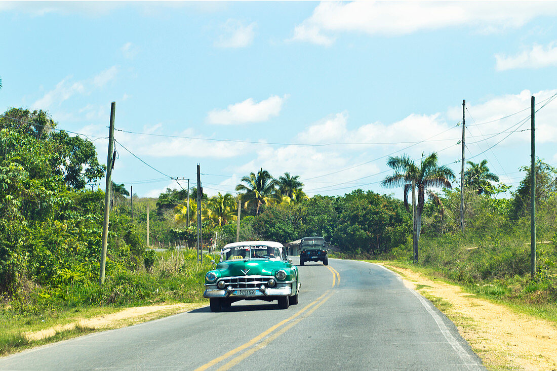 Classic green car driving through the Viñales Valley in Cuba