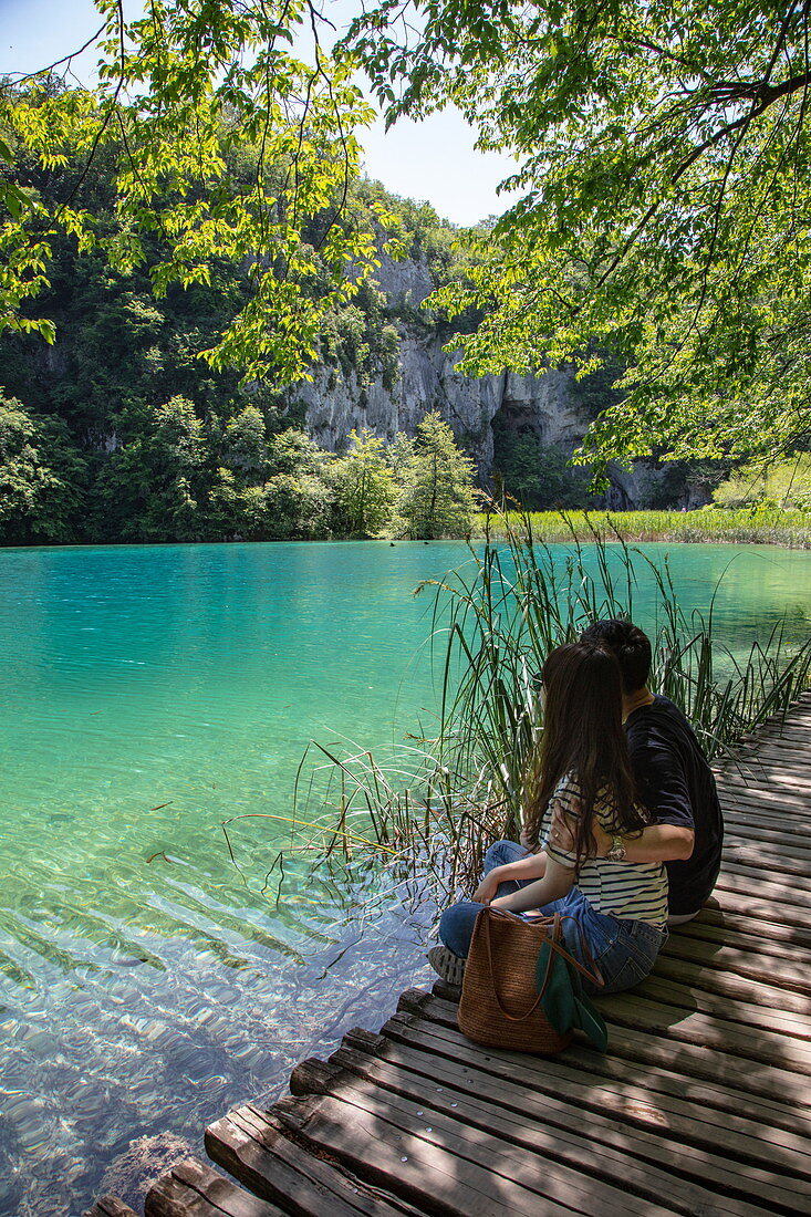 Couple sits on wooden plank path and admires clear water in a pool, Plitvice Lakes National Park, Lika-Senj, Croatia, Europe