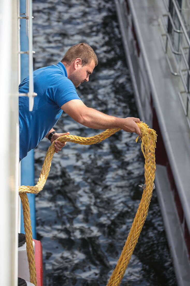 Matrose mit Seil an Bord von Flusskreuzfahrtschiff während einer Kreuzfahrt auf dem Rhein, Koblenz, Rheinland-Pfalz, Deutschland, Europa