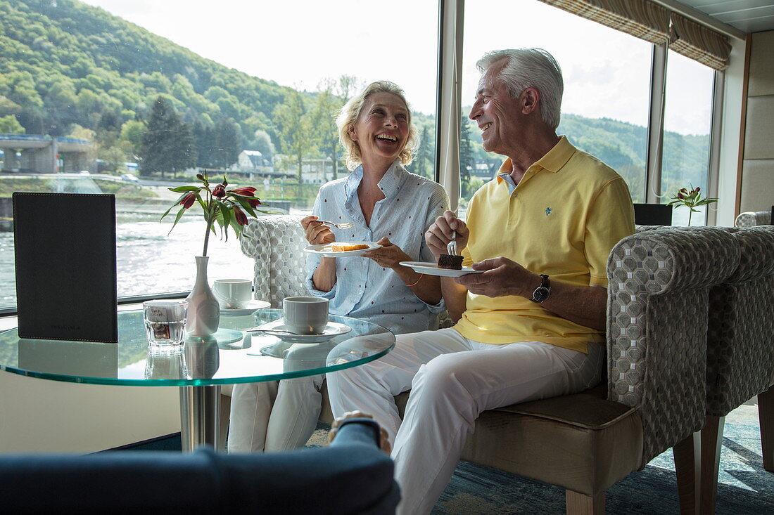 Paar genießt Nachmittagskaffee in der Panorama Lounge an Bord von Flusskreuzfahrtschiff während einer Kreuzfahrt auf dem Rhein, Goarshausen Wellmich, Rheinland-Pfalz, Deutschland, Europa