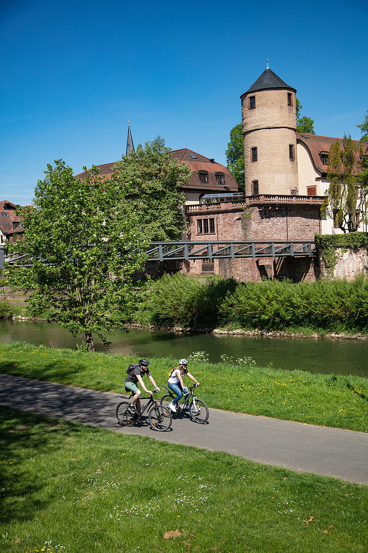 Cyclists on cycle path along the Tauber with the former Princely Court and White Tower of the city wall behind it, Wertheim, Spessart-Mainland, Franconia, Baden-Wuerttemberg, Germany, Europe