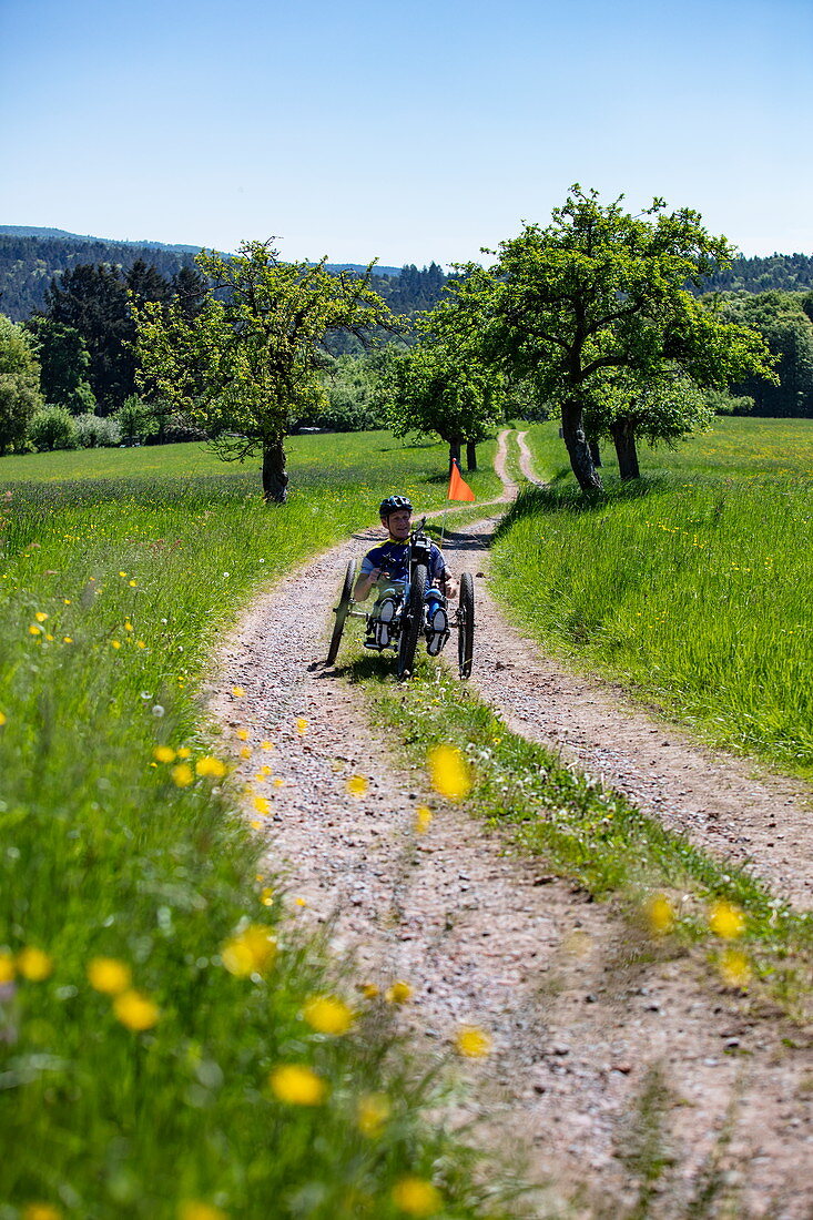 Man rides a bicycle for paraplegics on a dirt road through lush spring meadow, Heimbuchenthal, Räuberland, Spessart-Mainland, Franconia, Bavaria, Germany, Europe